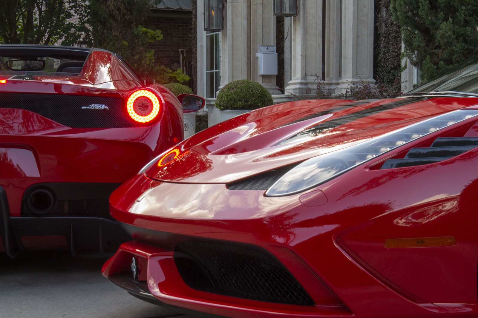 Reflections across the glossy red nose of a Ferrari 458 Speciale, a Speciale Aperta's taillight glowing behind it