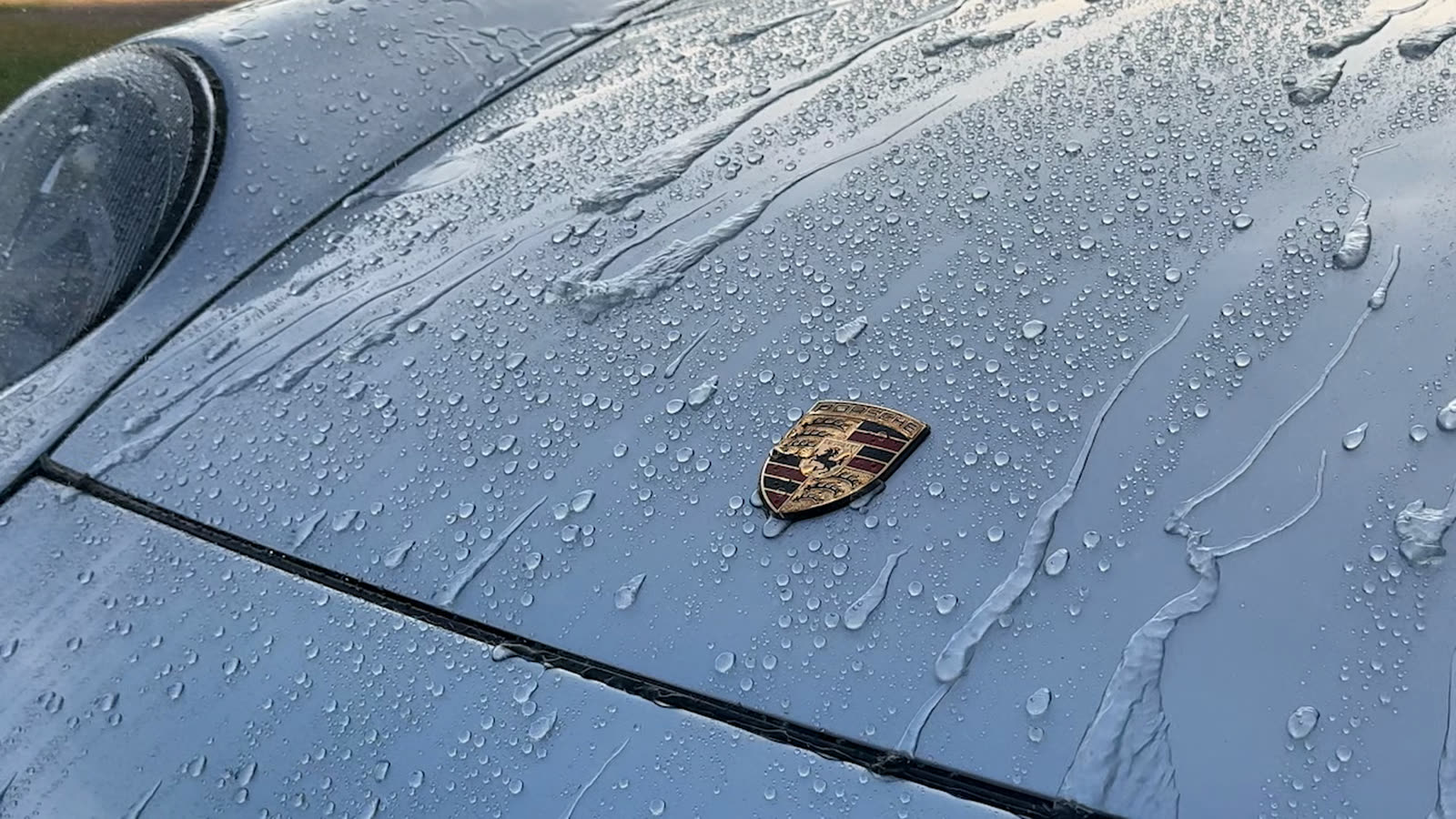 Water beading and sheeting around the crest on the coated silver hood of a Porsche 911