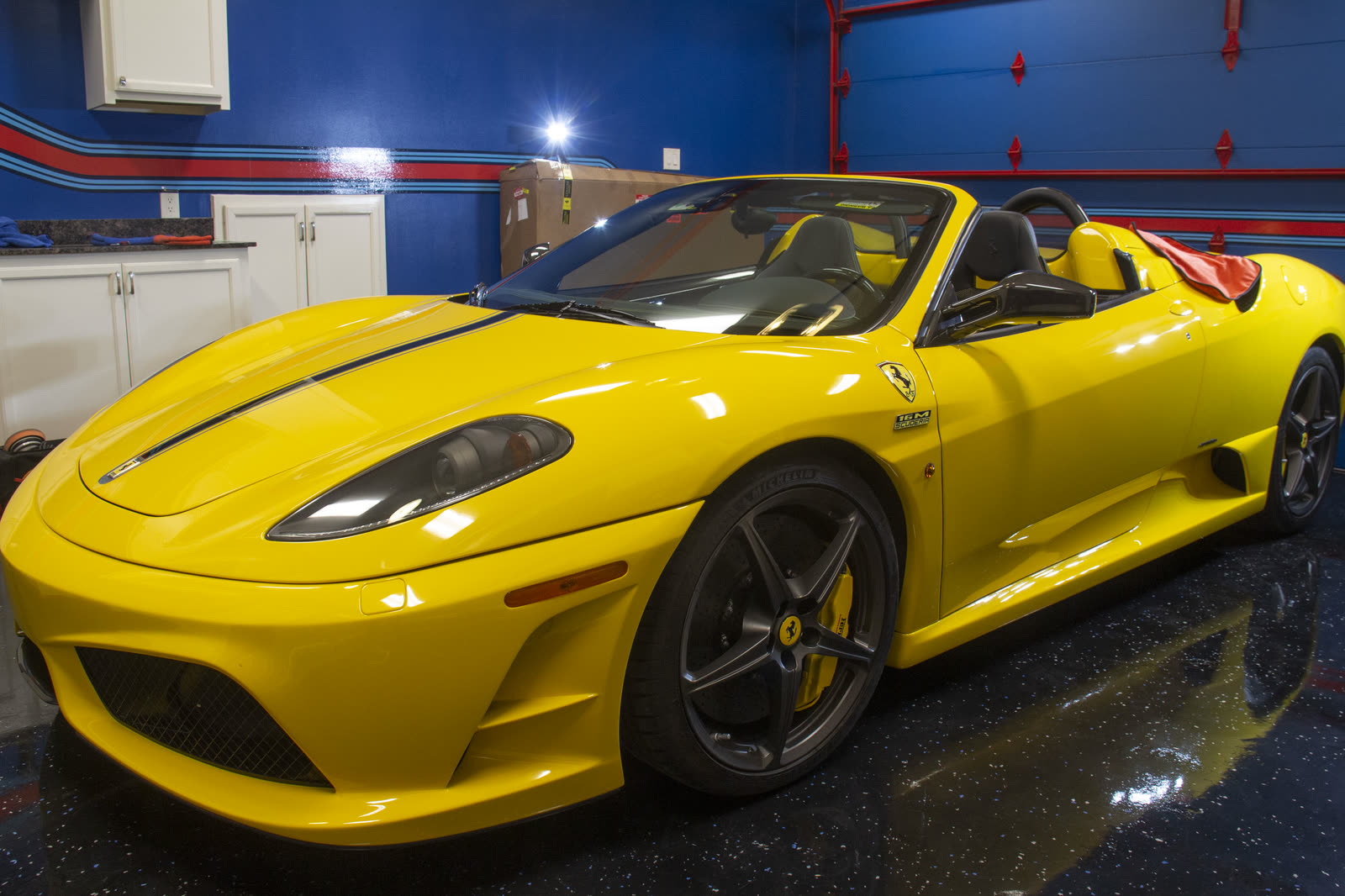 A glossy yellow Ferrari F430 Scuderia Spider reflected in the shop floor