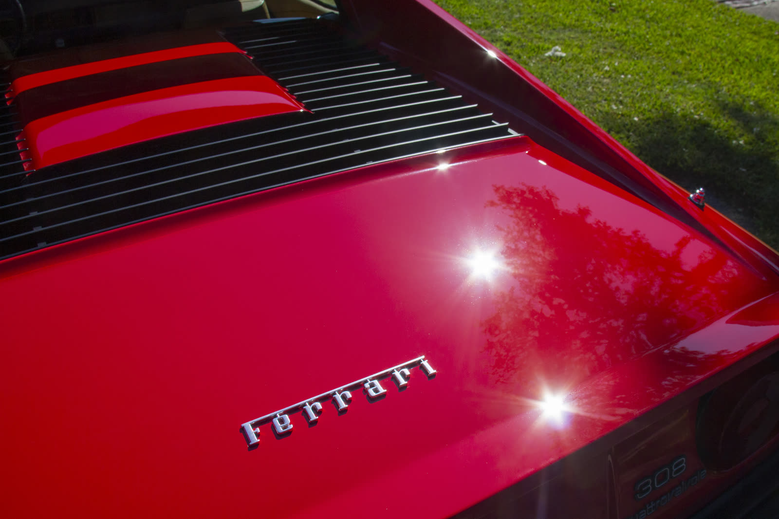 Corrected red paint on the engine lid of a Ferrari 308, with the Ferrari script in the sun