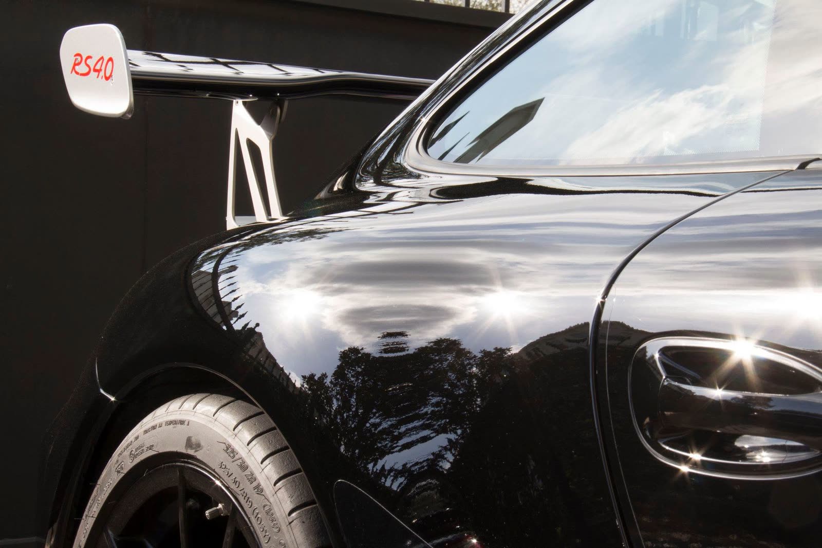 The sun on the black rear flank of a Porsche 911 GT3 RS 4.0, below its wing