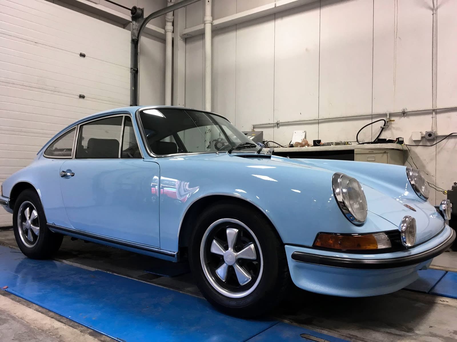 A pale blue classic Porsche 911 on Fuchs wheels in the shop